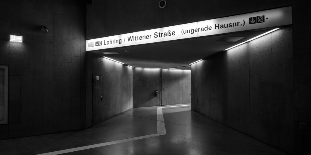 Schwarz-weiss Foto vom Zwischengeschoß der U-Bahnstation Bochum Lohring. Ein Wegweiser an der Decke zum Ausgang zeigt den Schriftzug: Lohring / Wittener Straße (ungerade Hausnummern)