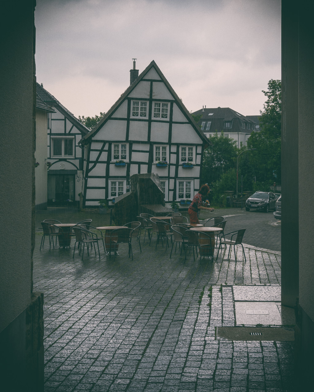 Eine Frau räumt im strömenden Regen die Tische eines Cafés ab.